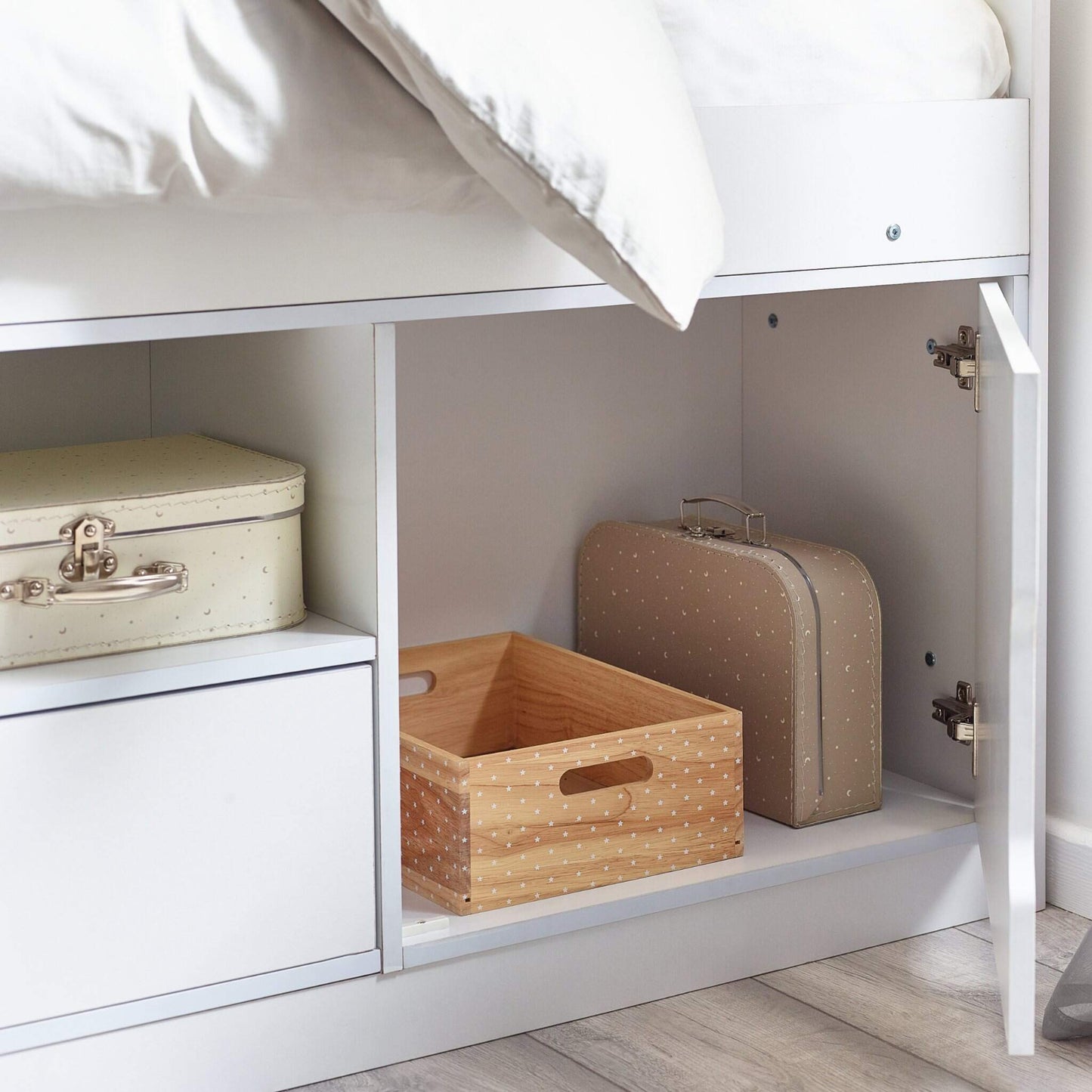 Storage compartments under a bed with a wooden box, beige suitcase, and metal trunk.