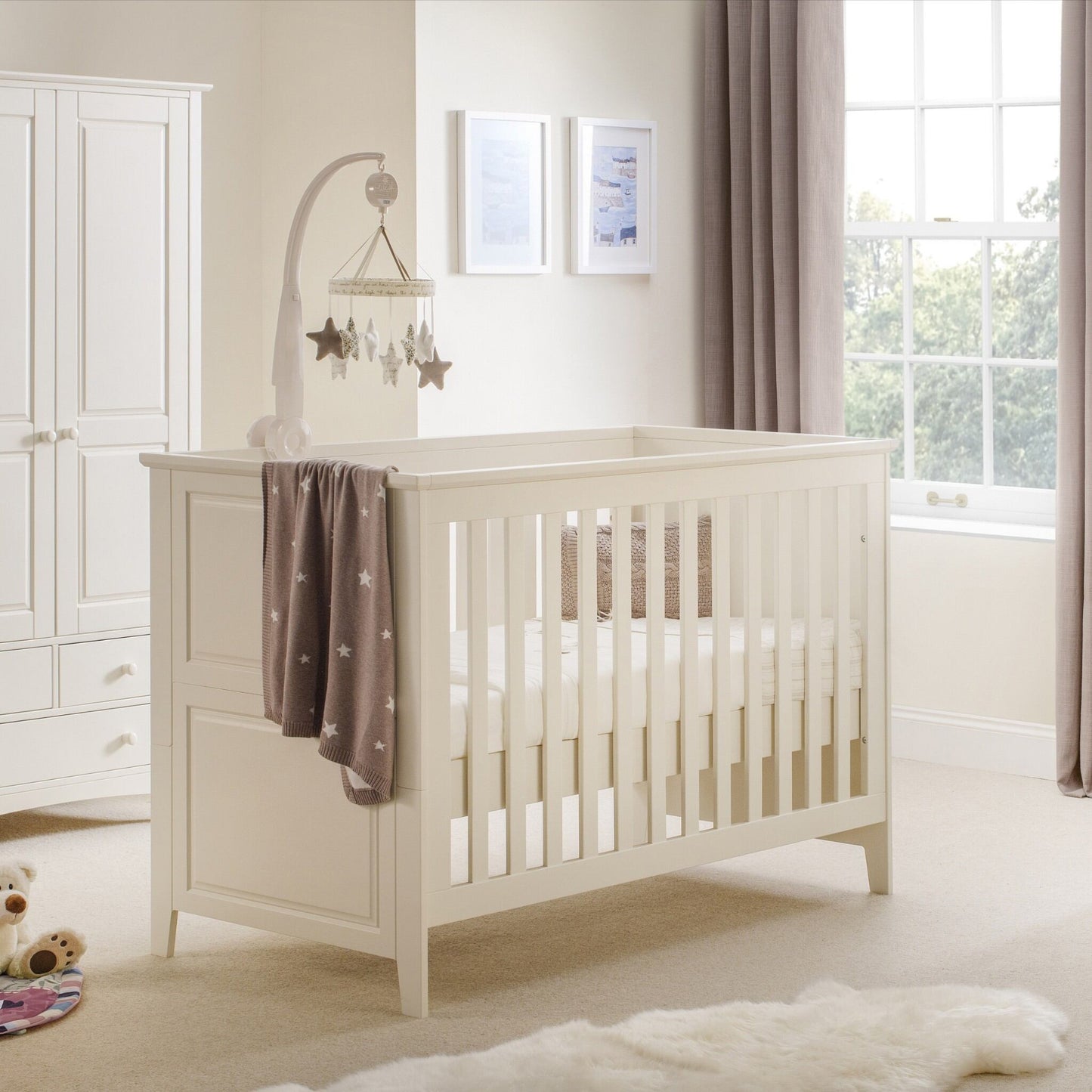 Cameo convertible cot bed in stone white with a solid pine frame, in a nursery setting next to a matching wardrobe.