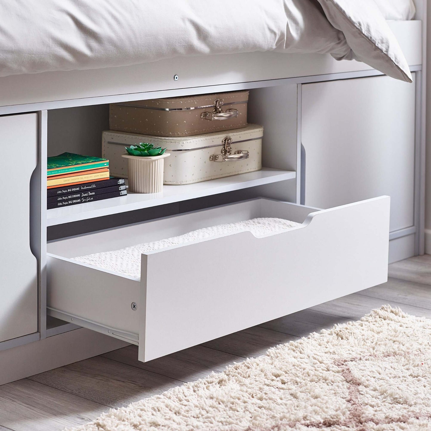 Underbed storage drawer with suitcases and books in a bedroom setting
