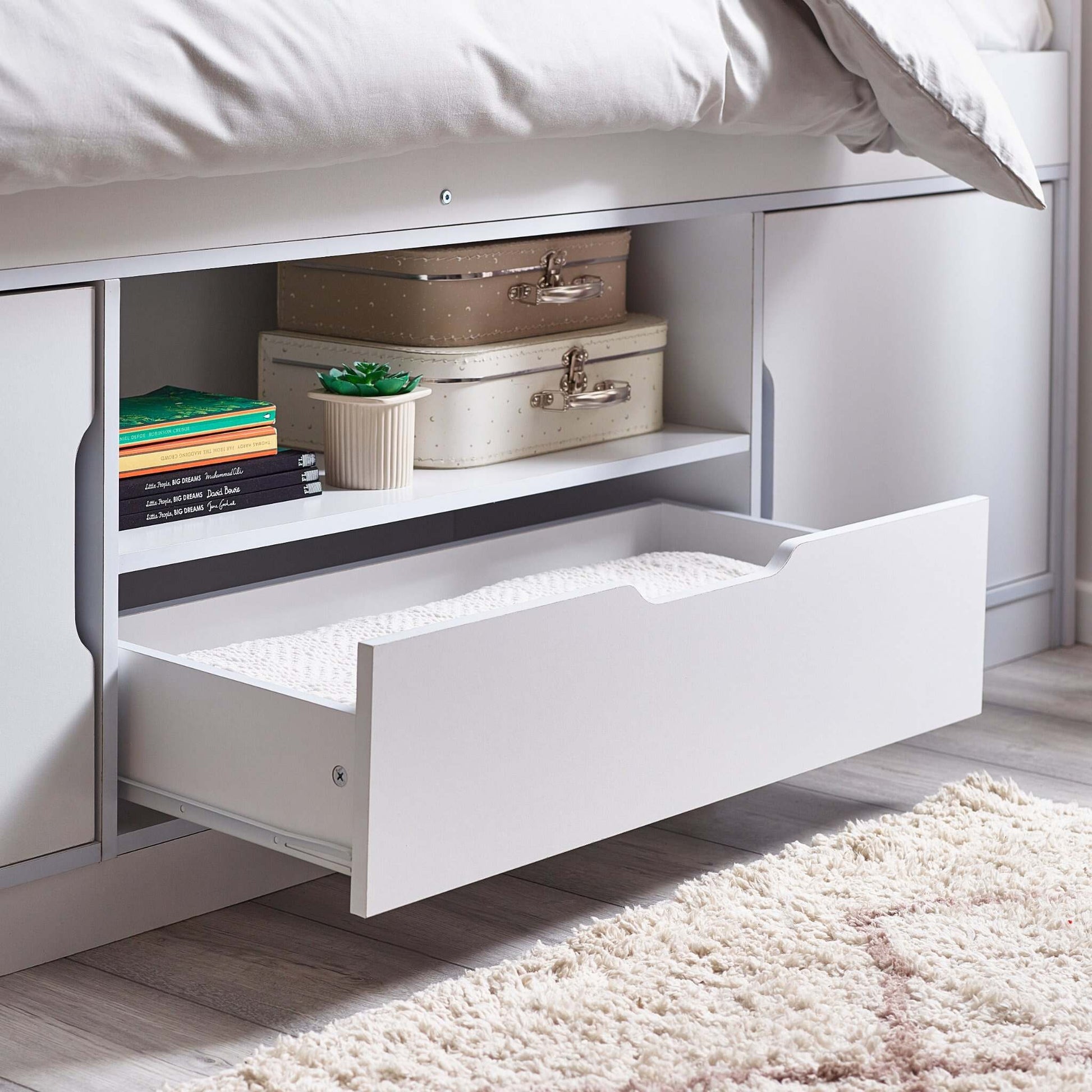 Underbed storage drawer with suitcases and books in a bedroom setting