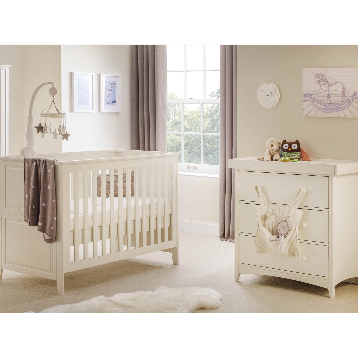 The Cameo Cotbed and matching Changing Station finished in stone white, displayed in a cream nursery room with fluffy toys.